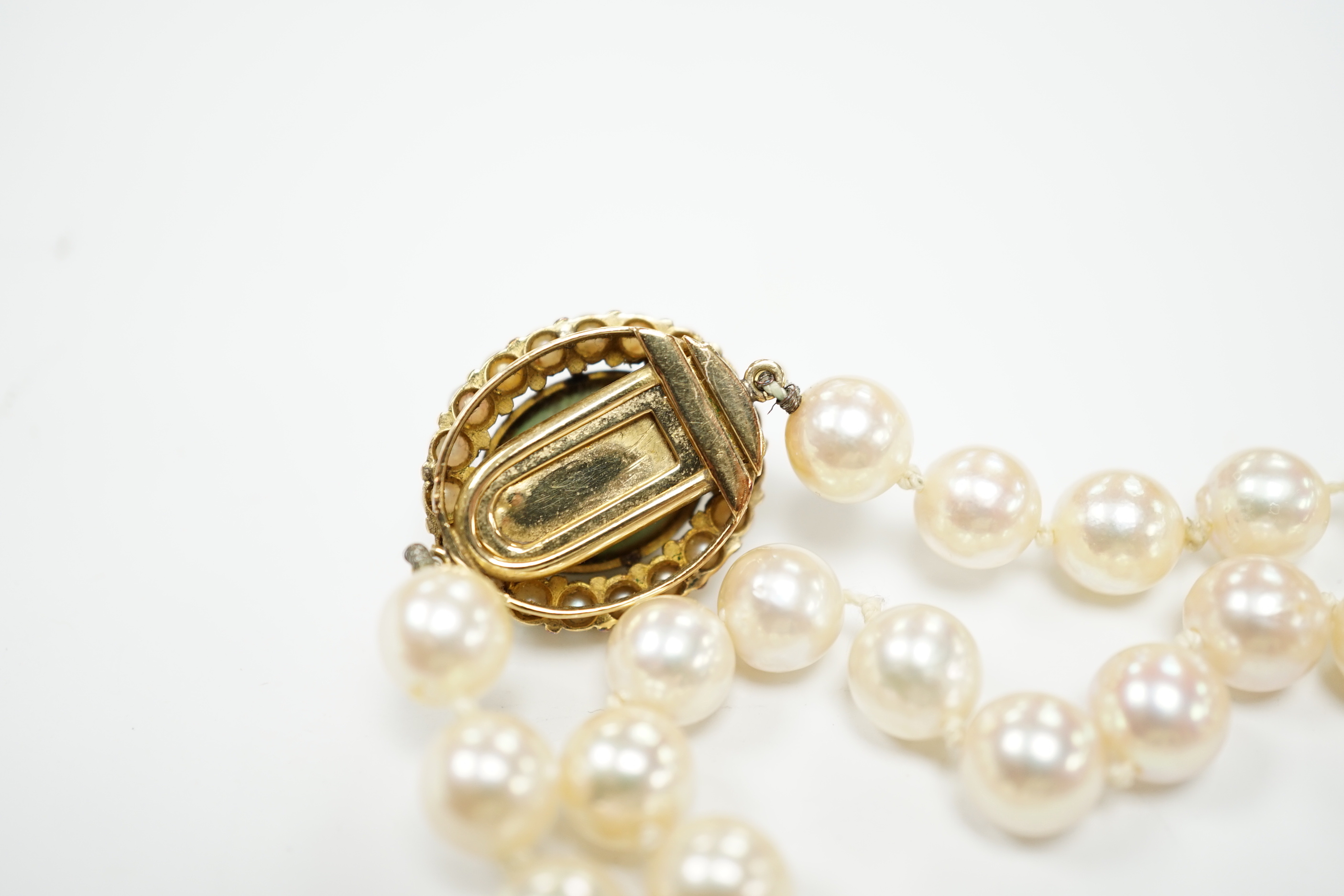 A Portuguese single strand cultured pearl necklace, with cabochon nephrite and seed pearl cluster set yellow metal clasp, 86cm.